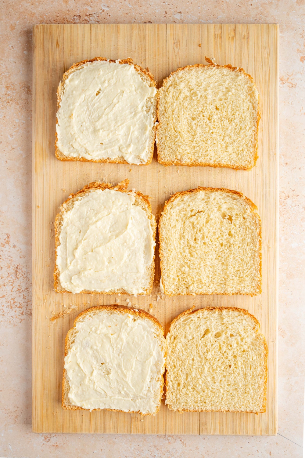 A wooden board with six slices of bread with half spread with a whipped cream cheese mixture. The board is on a tan counter.