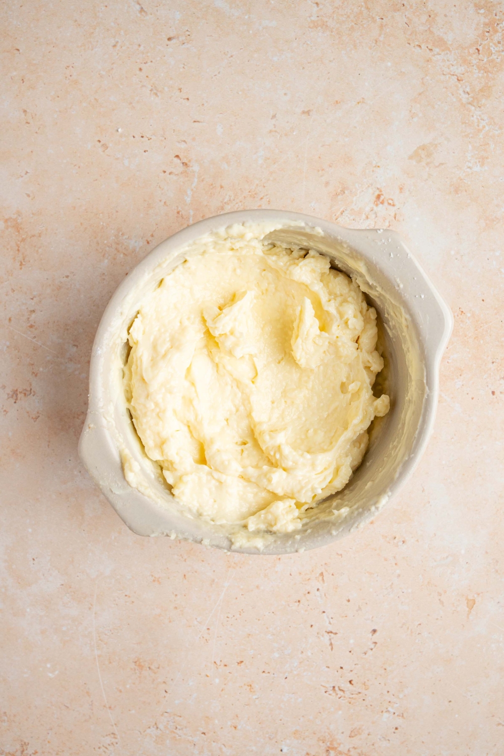 A white bowl with whipped cream cheese mixed with powdered sugar. The bowl is on a tan counter.