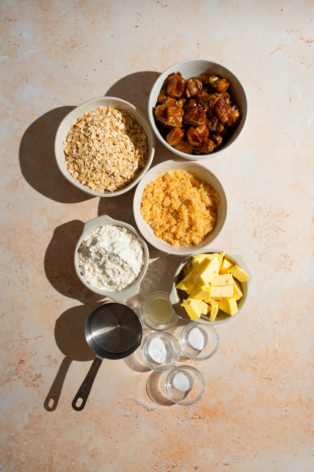 An overhead shot of several bowls in various sizes containing ingredients to make old fashioned date bars including dates, oats, brown sugar, butter, baking powder, lemon juice, and more.