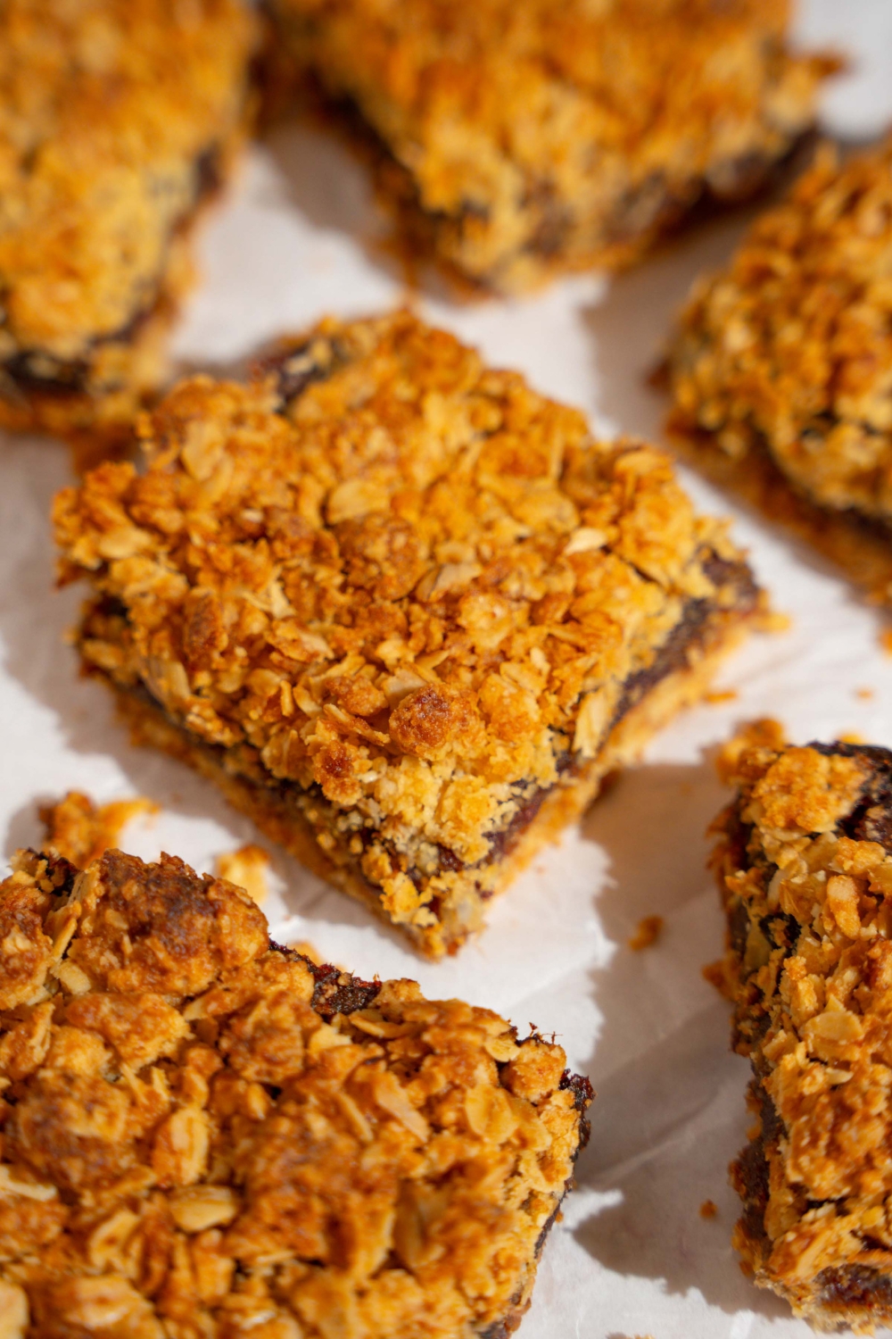 Several old fashioned date bars on a piece of parchment paper on a tan counter.