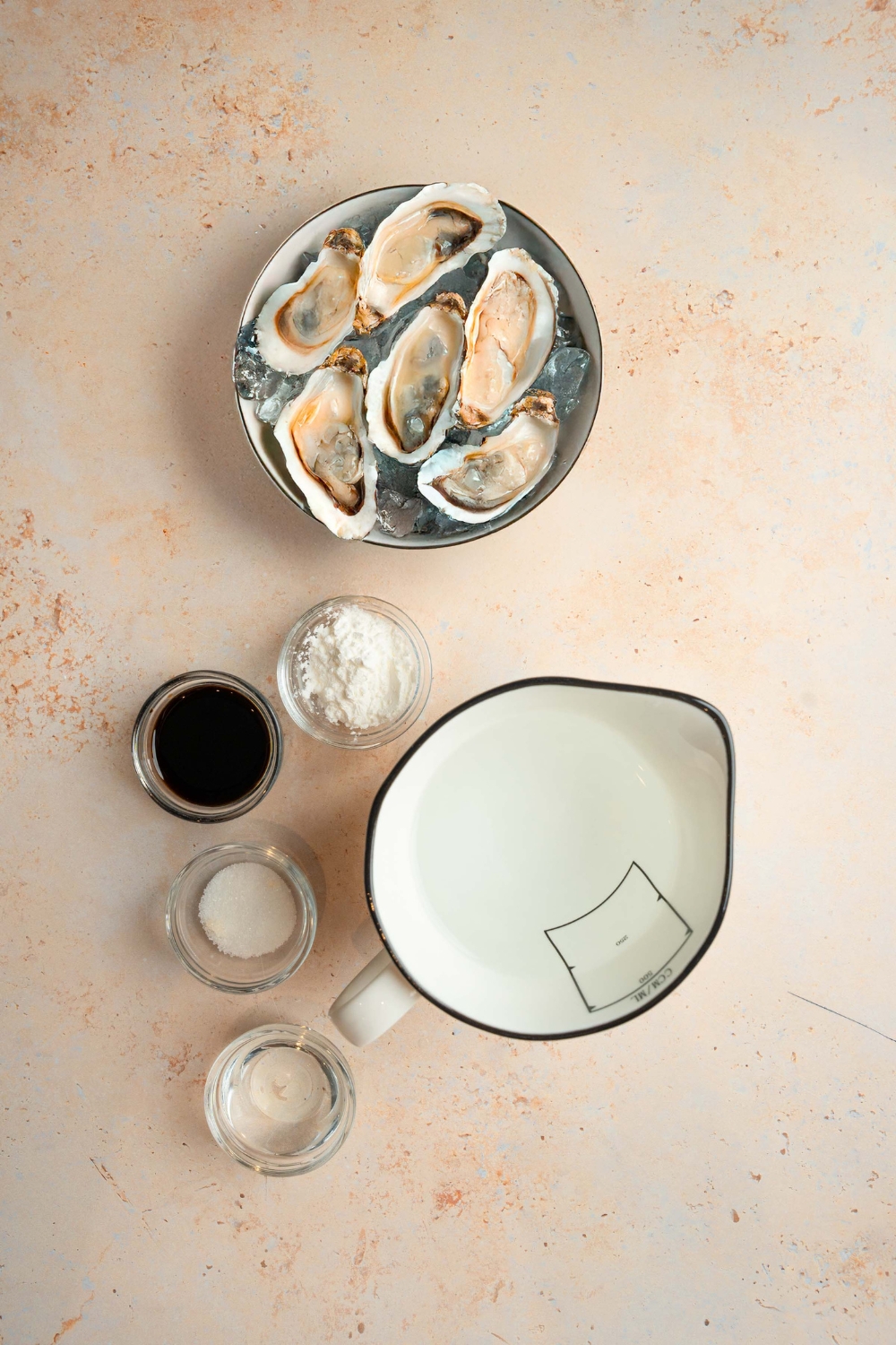 An overhead shot of several bowls in various sizes containing ingredients to make oyster sauce including oysters on ice, water, soy sauce, corn starch, and sugar.