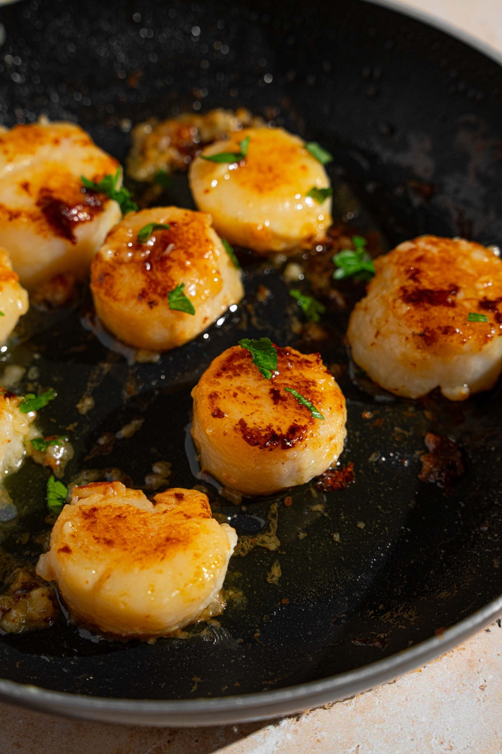 Pan seared scallops in a skillet with butter and garlic, garnished with fresh parsley.