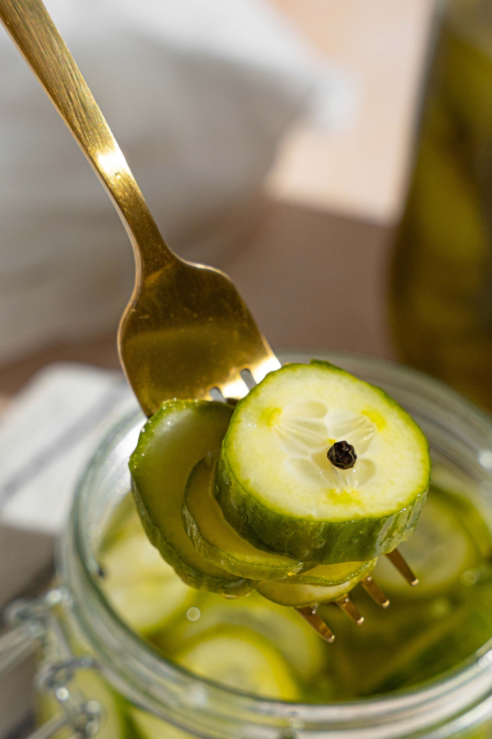 A close up of a fork with sliced quick pickles. There is a jar of pickles on a tan counter blurred in the background.