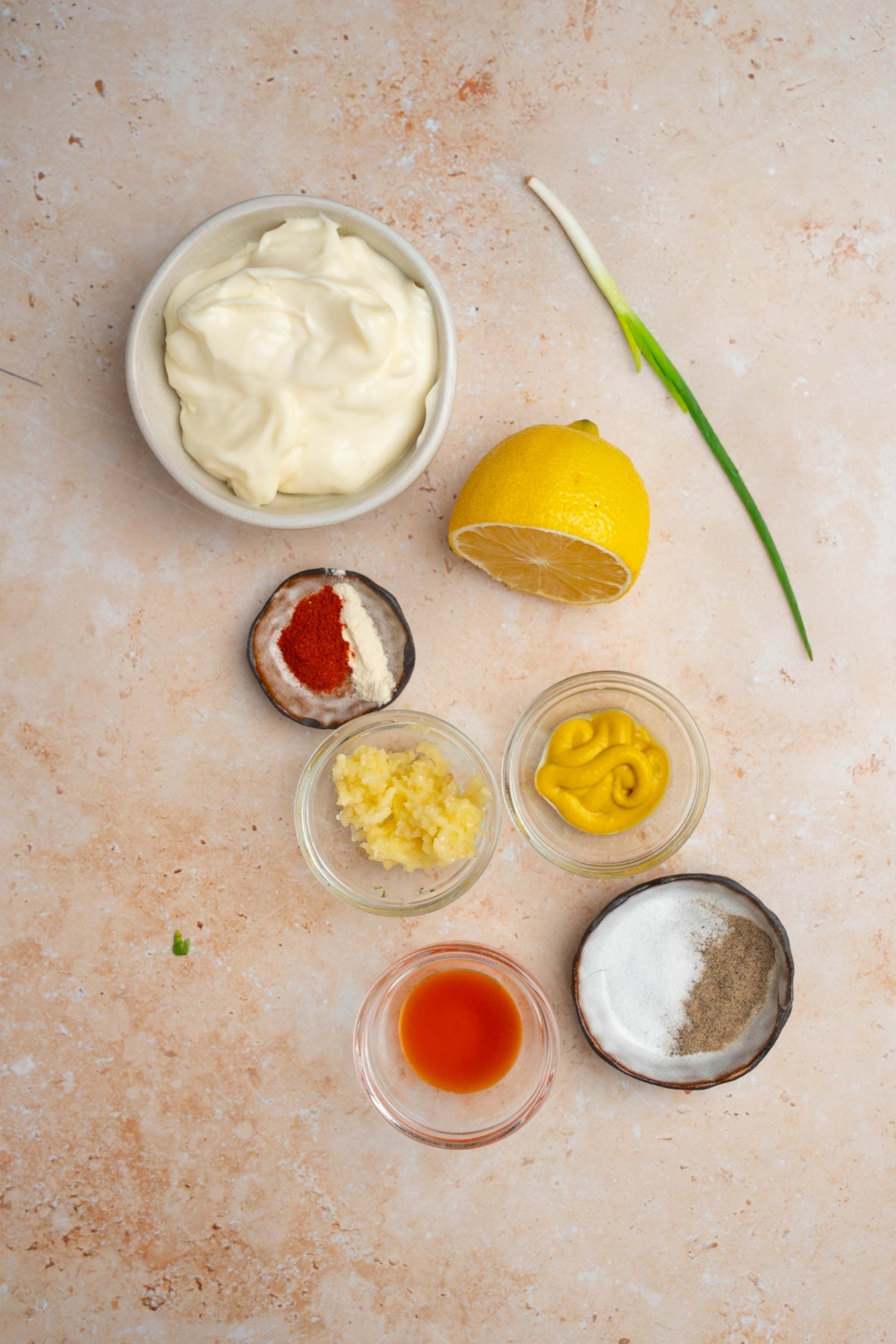 An overhead shot of several bowls in various sizes containing ingredients to make remoulade sauce including mayo, mustard, hot sauce, lemon, and seasonings.