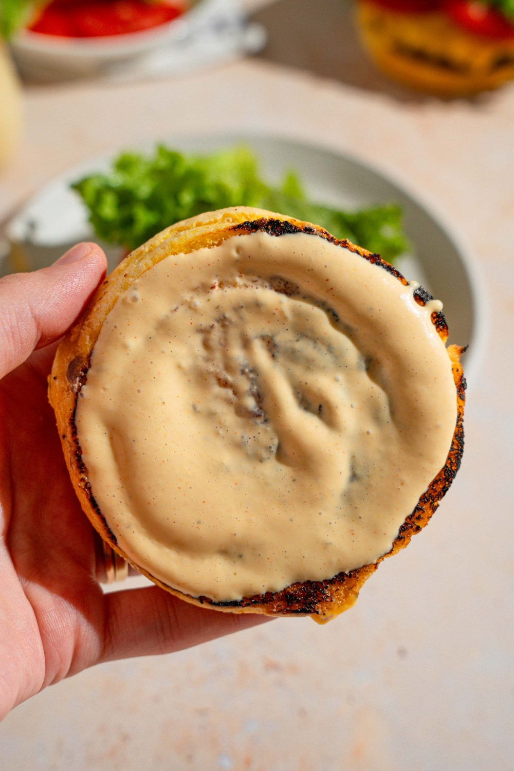 A close up of a hand holding the top of a bun smeared with Shake Shack sauce. There is a white plate on a tan counter blurred in the background.