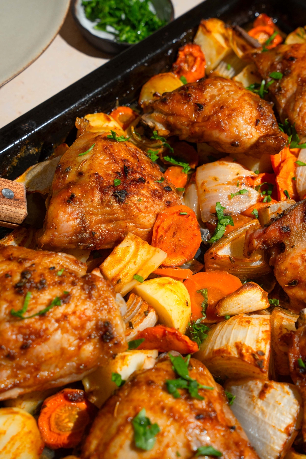 A baking sheet with roasted chicken thighs, carrots, potatoes, and onions garnished with fresh parsley.