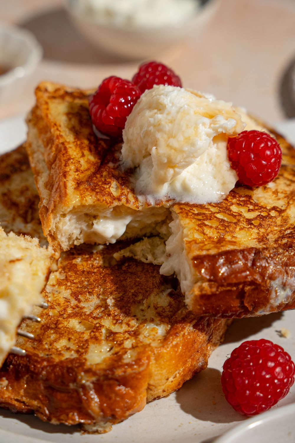 A white plate with stuffed french toast topped with whipped cream cheese and raspberries.