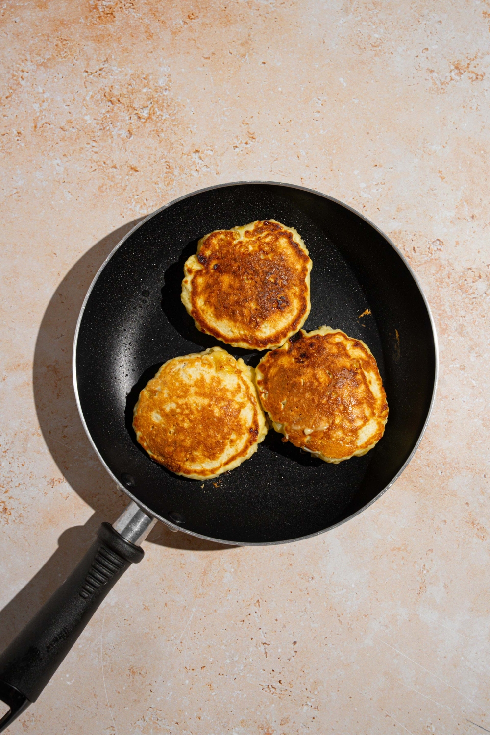 A skillet with three 3 ingredient banana pancakes. The skillet is on a tan counter.