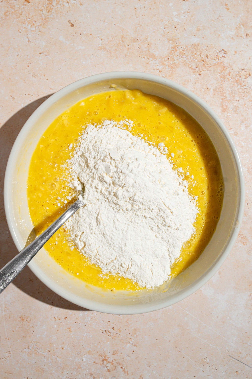 A white bowl with a fork mixing 3 ingredient banana pancake batter. The bowl is on a tan counter.