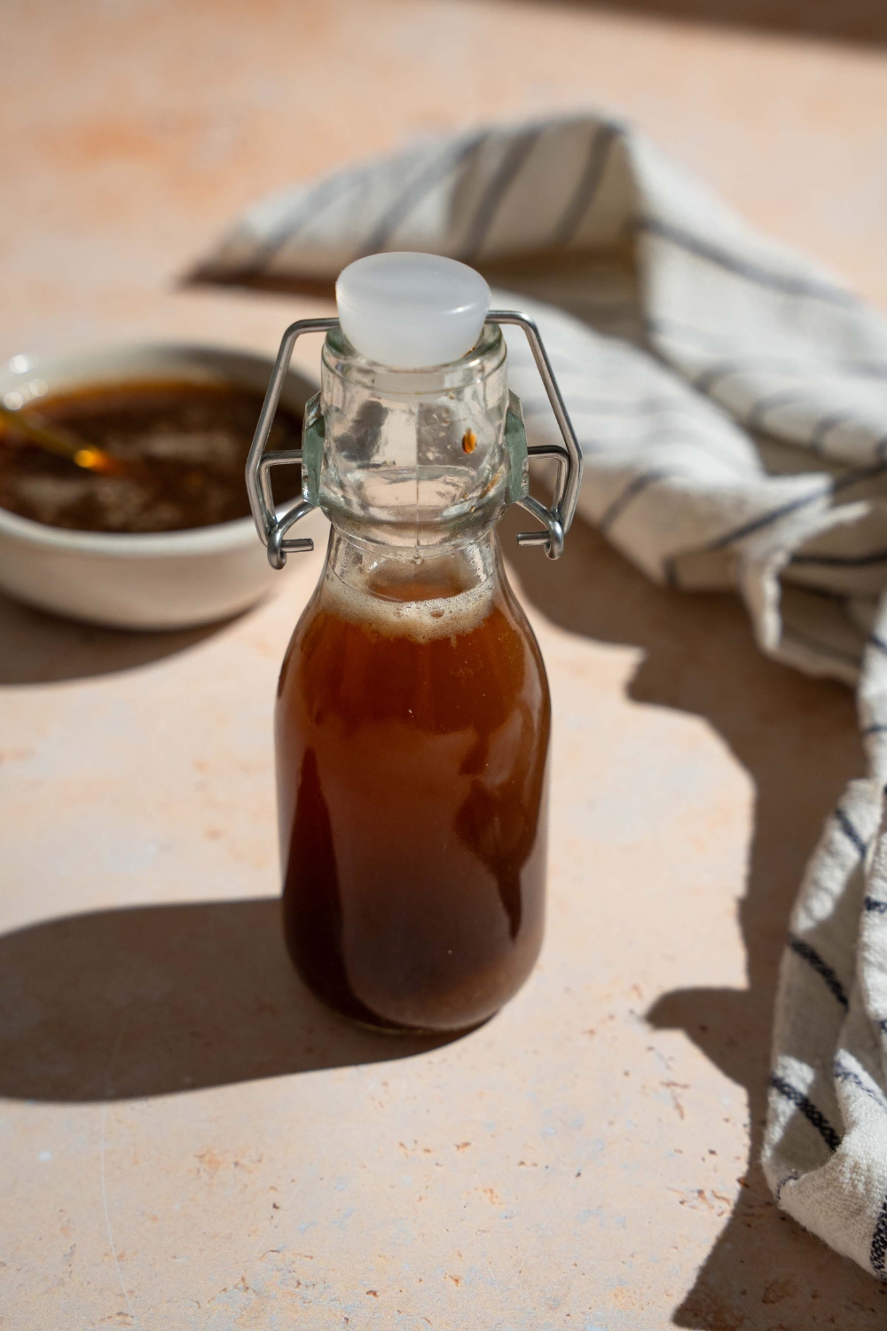 A sealed jar of oyster sauce on a tan counter with a white striped napkin and bowl of sauce.