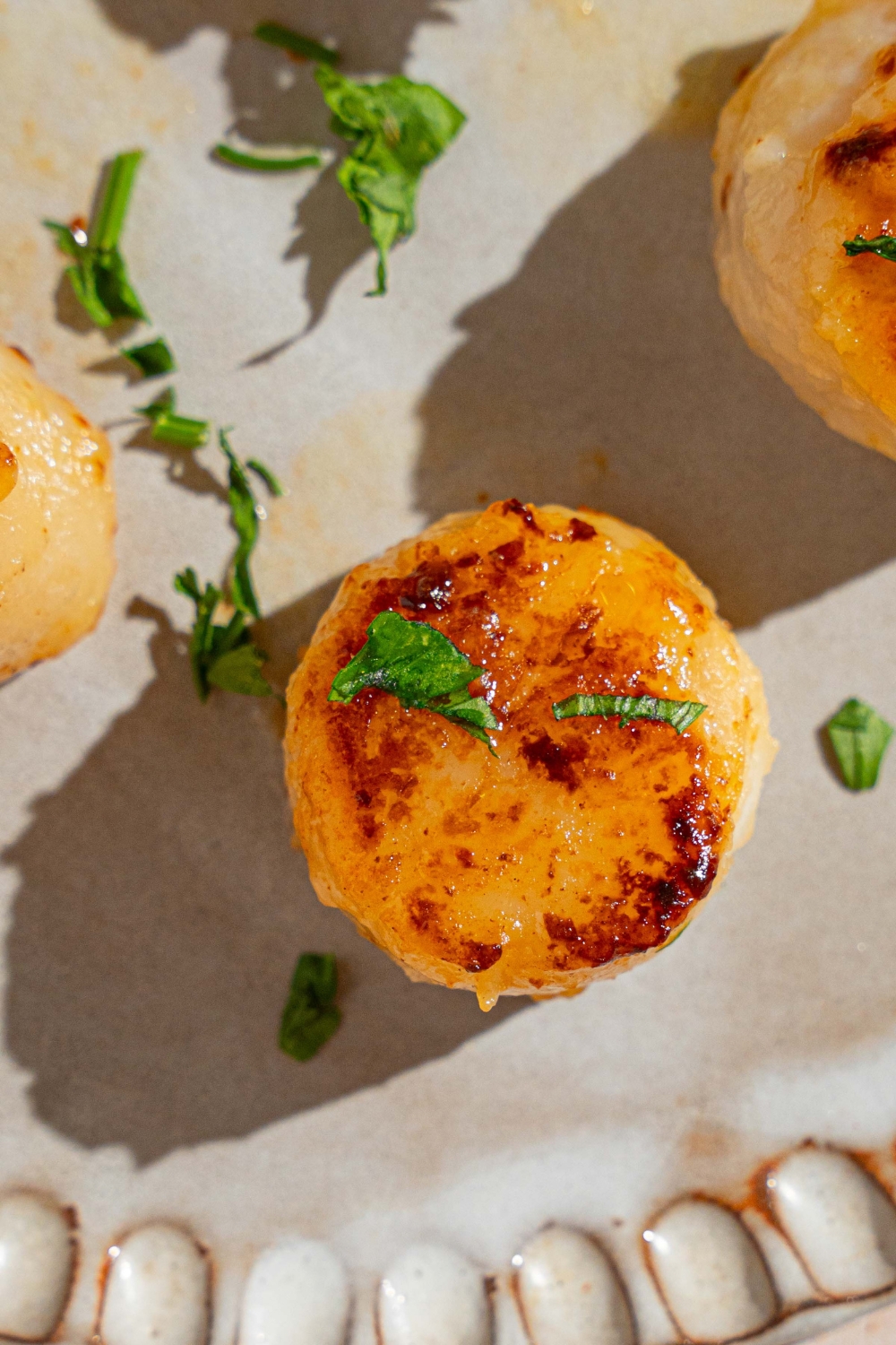 A ceramic plate with several pan seared scallops garnished with fresh parsley.