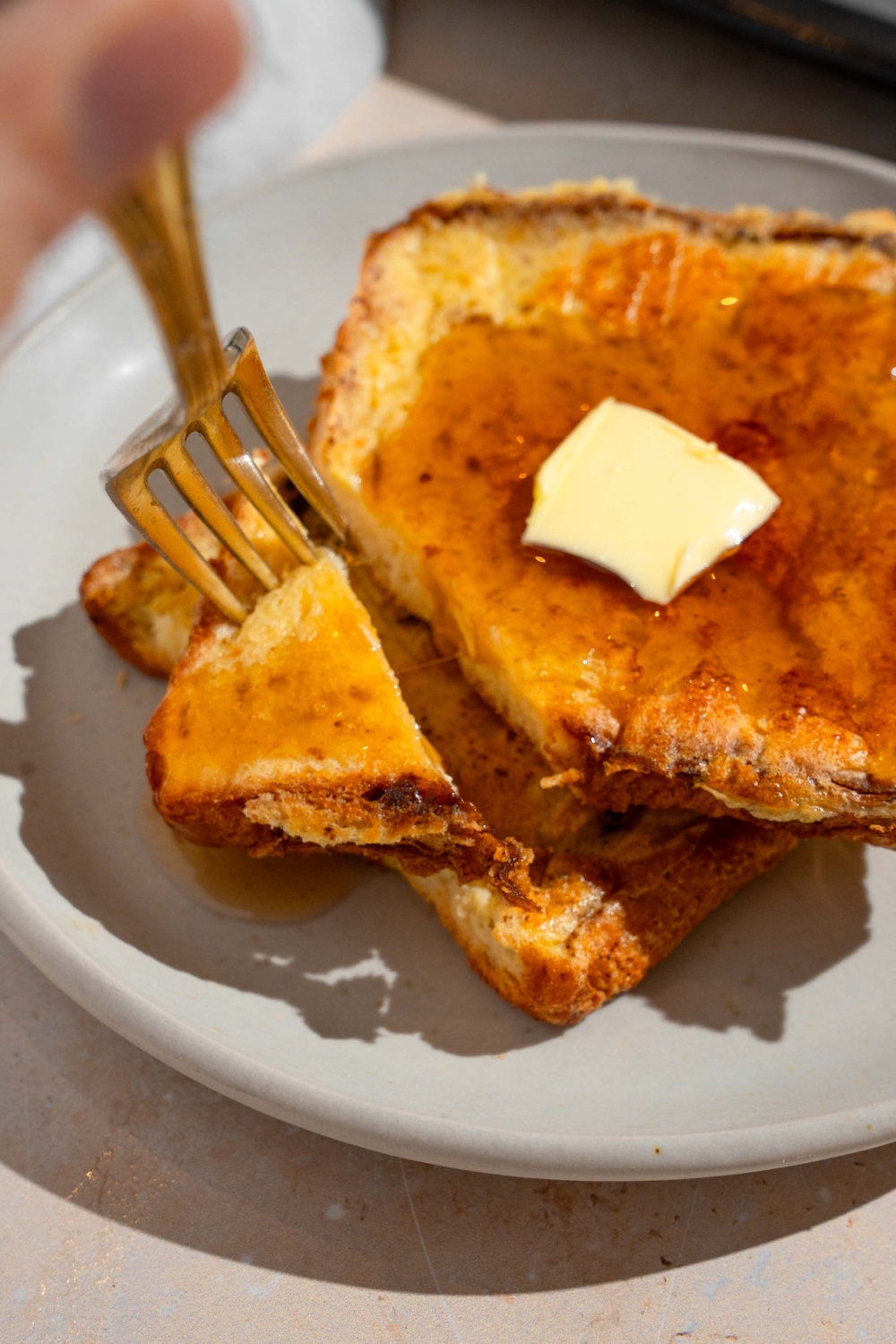 A plate with two slices of sheet pan french toast topped with butter and drizzled with syrup. There is a fork taking a bite of french toast.