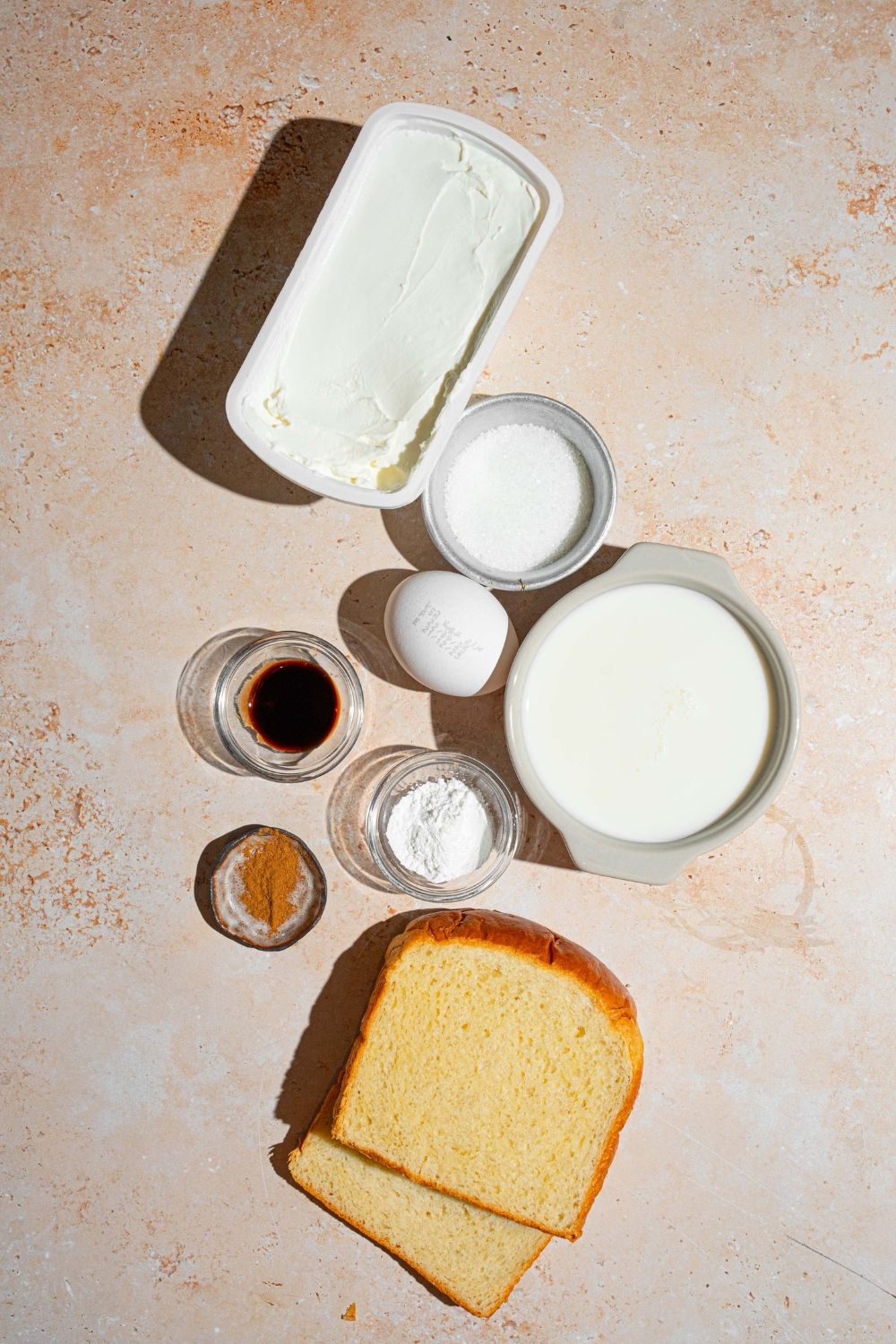 An overhead shot with several bowls in various sizes containing ingredients to make stuffed french toast including cream cheese, powdered sugar, brioche bread, milk, sugar, and egg.