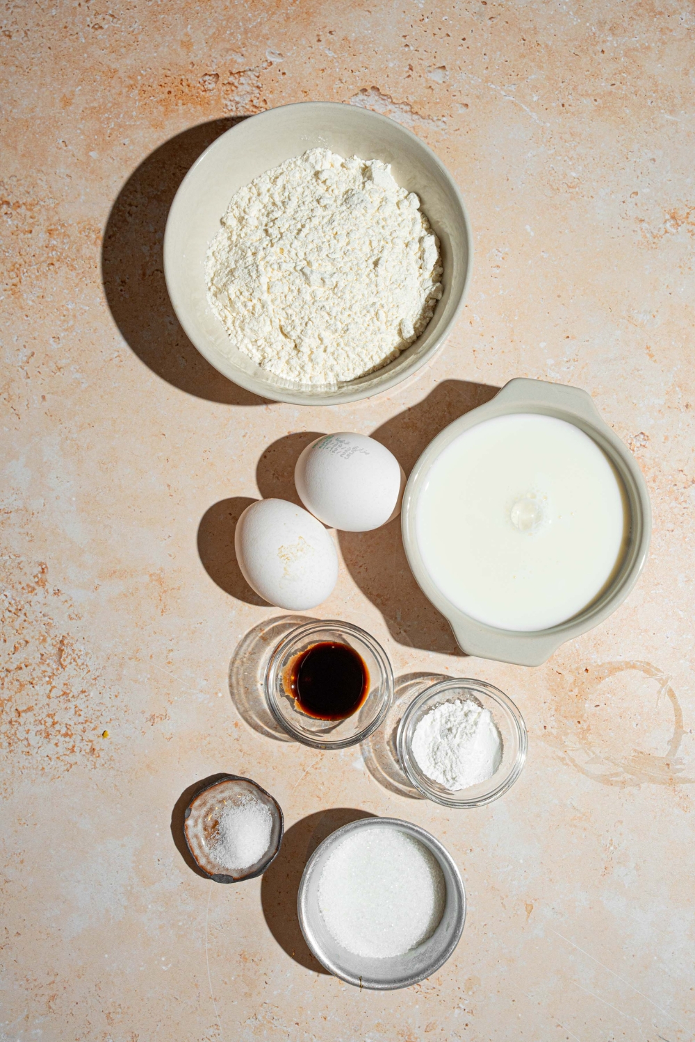 An overhead shot of several bowls in various sizes containing ingredients to make sweet cream fluffy pancakes including flour, heavy cream, eggs, vanilla, and salt.