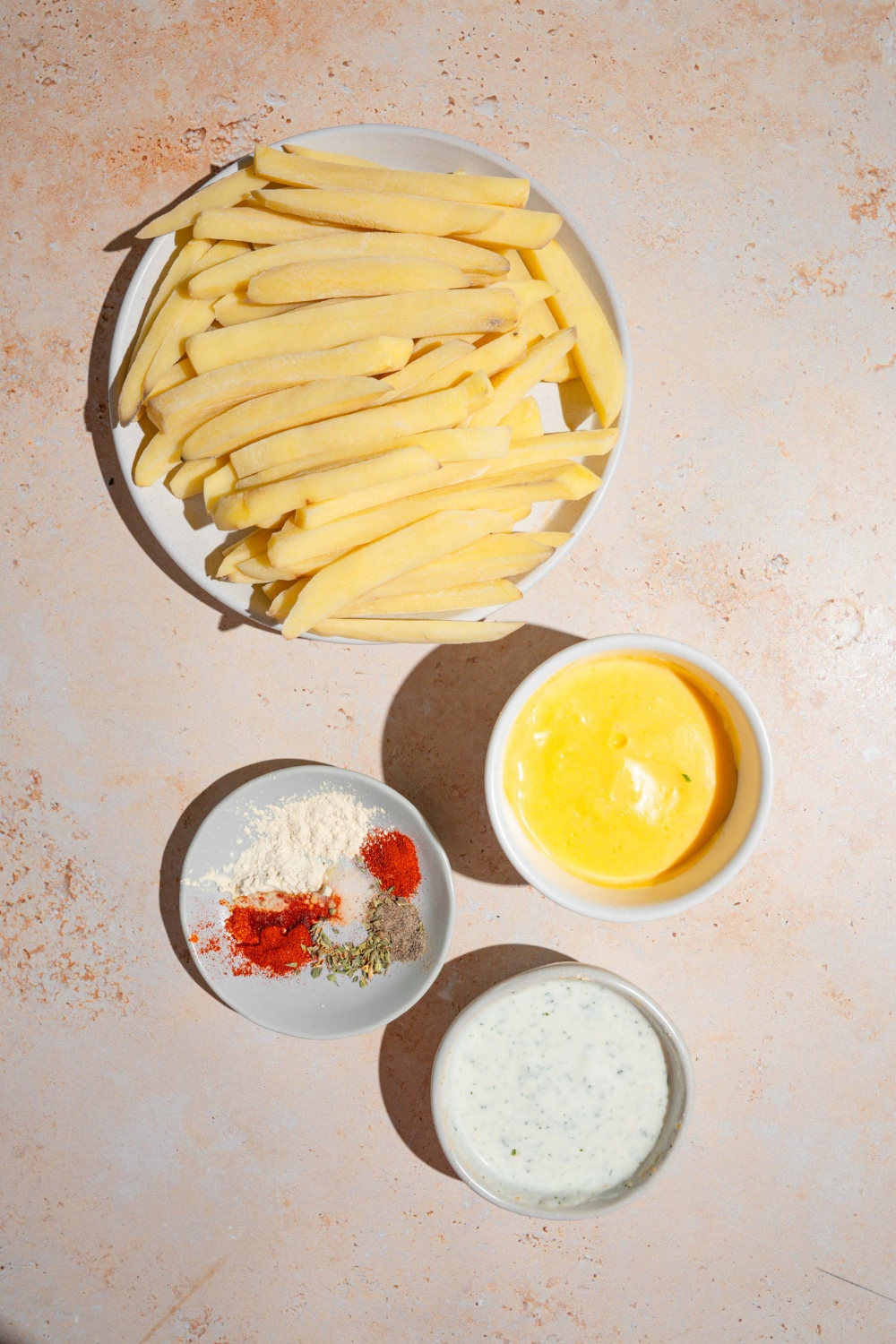 An overhead shot of several bowls in various sizes containing ingredients to make copycat Wingstop Voodoo fries including fries, cheese sauce, ranch dressing, and seasonings.