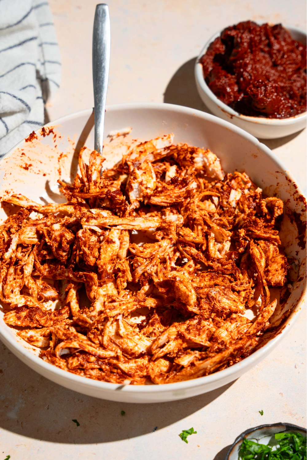 Shredded chicken adobo in a white bowl. A white cup filled with the adobo sauce is behind it.