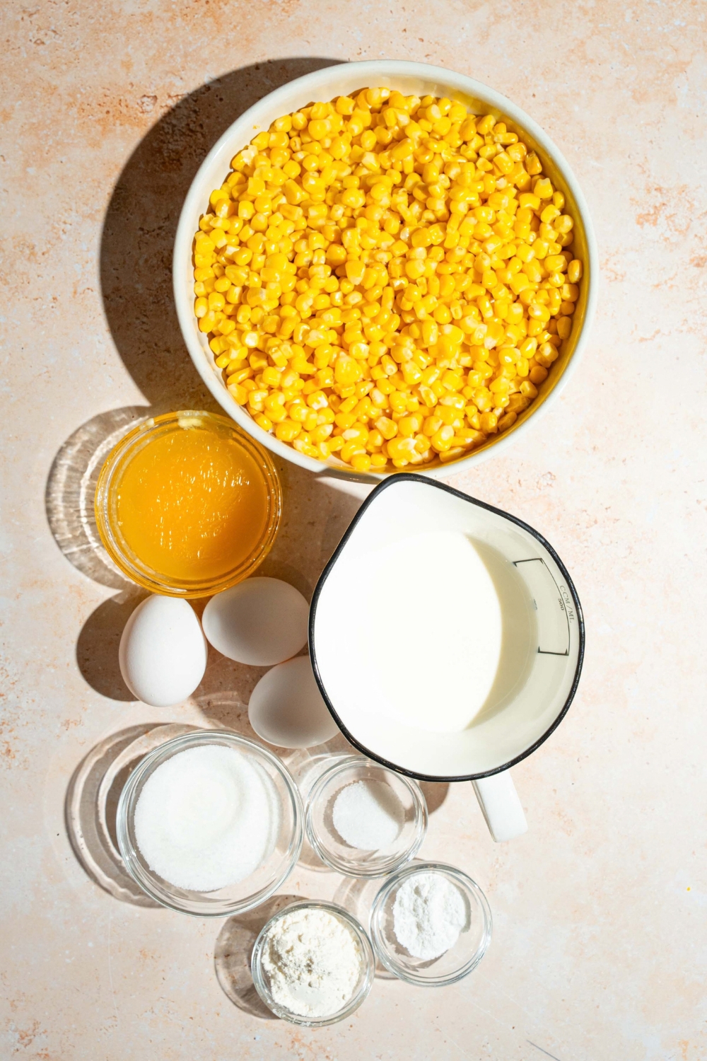 A bowl of corn, a bowl of melted butter, three eggs,
