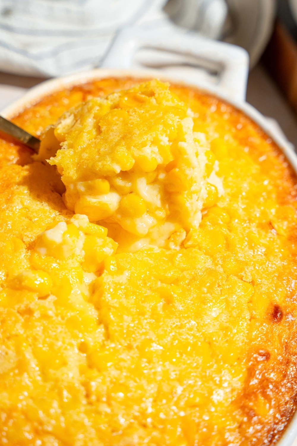 A scoop of corn casserole being pulled from a casserole dish that is filled with the casserole dish.