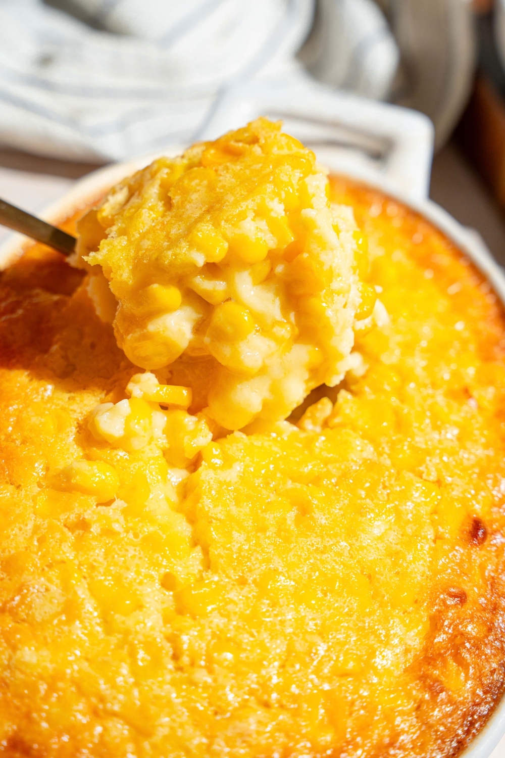 A big scoop of corn casserole being pulled from a casserole dish filled with the corn casserole.