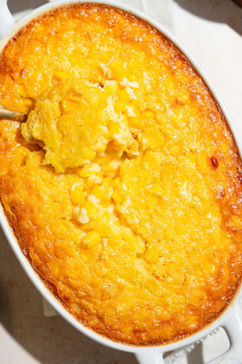 Corn casserole in a casserole dish with a scoop being pulled out of it.
