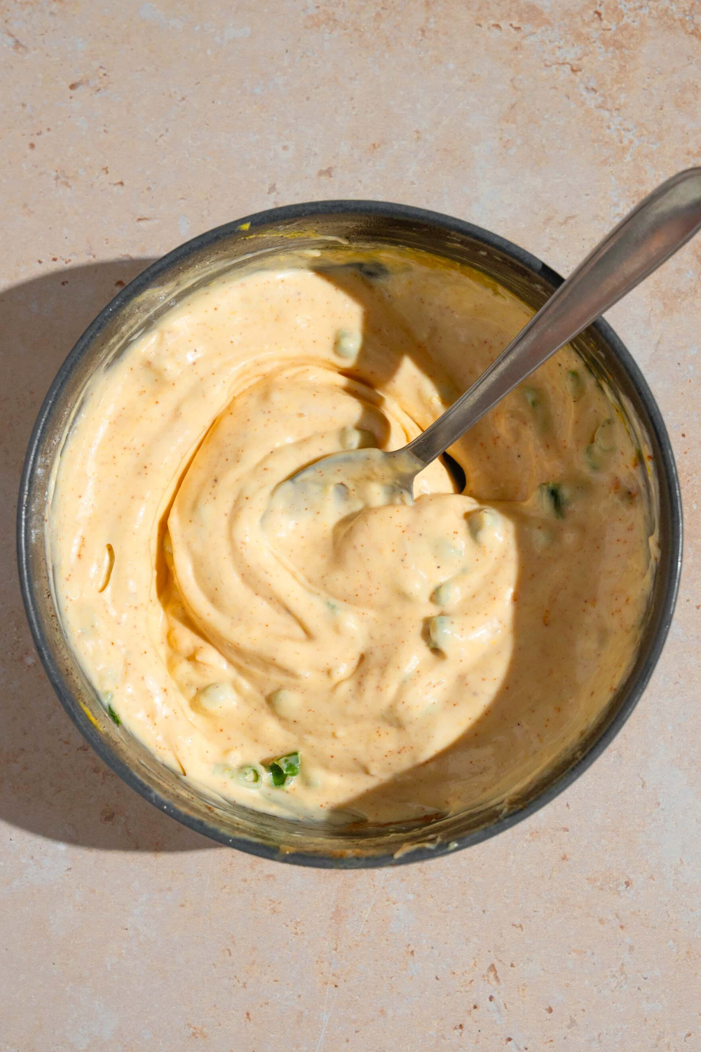 A spoon submerged in a bowl of remoulade sauce on a white counter.