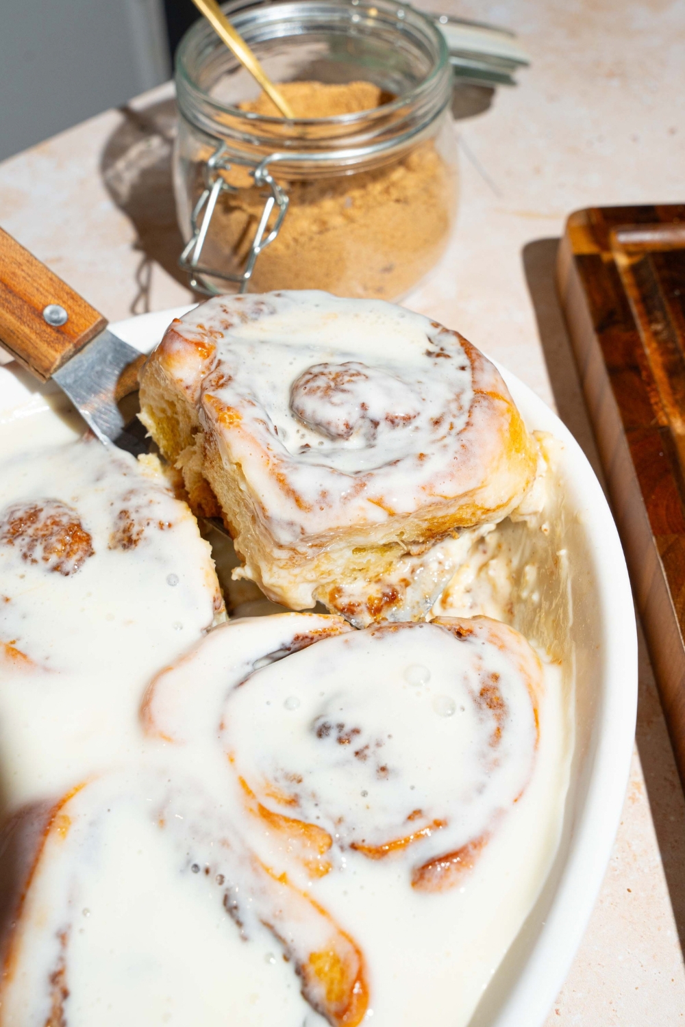 Heavy cream cinnamon rolls in a white baking dish with more heavy cream cinnamon rolls.
