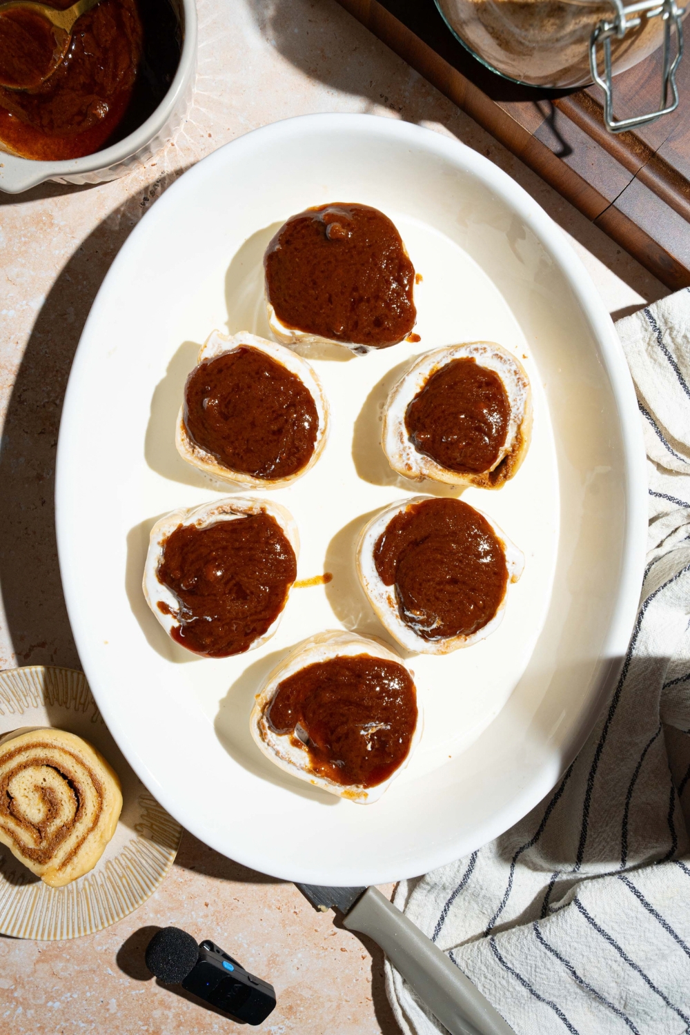 A dollop of brown sugar cinnamon mixture on top of six cinnamon rolls in a baking dish with heavy cream.