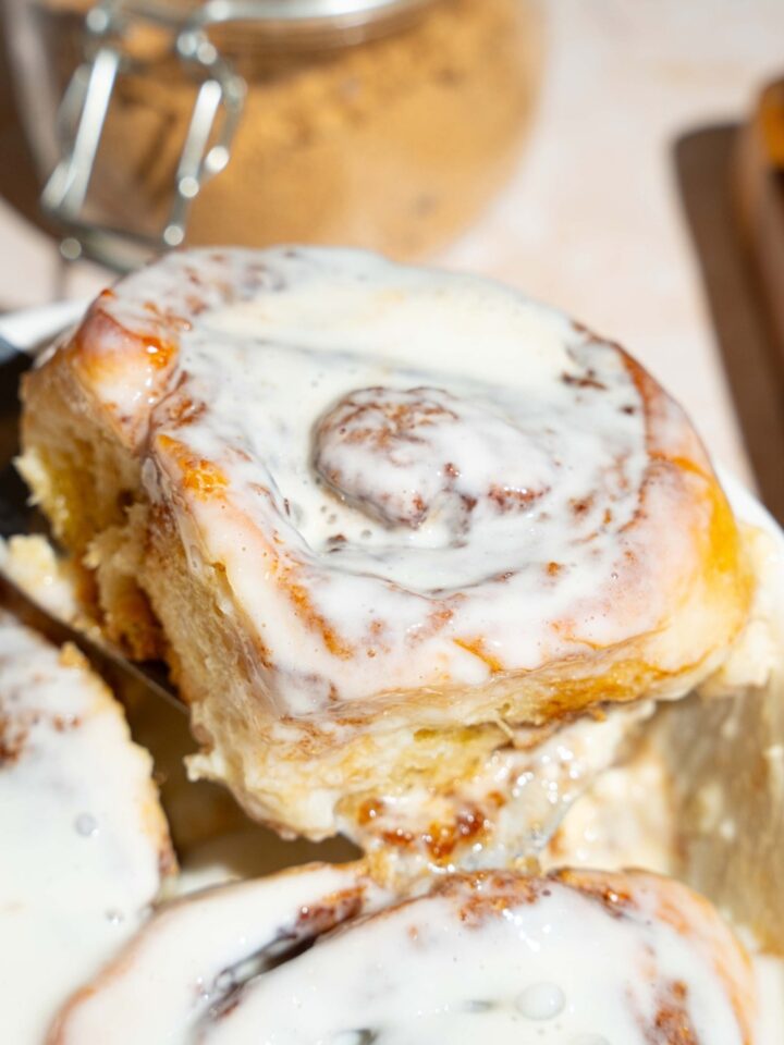 A cinnamon roll with heavy cream in front of some more baked heavy cream cinnamon rolls.