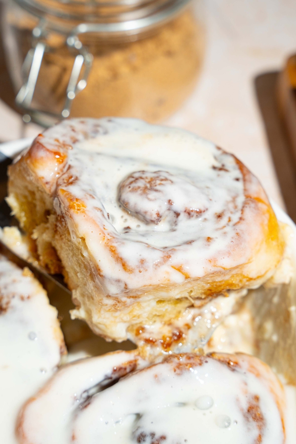 A cinnamon roll with heavy cream in front of some more baked heavy cream cinnamon rolls.