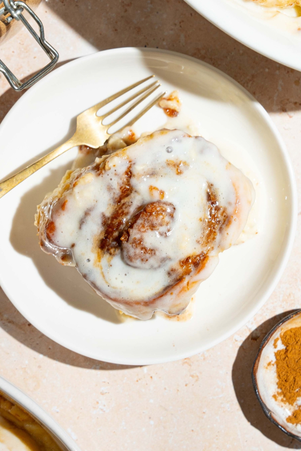 A cinnamon roll with heavy cream on top of a white plate with a gold fork on it.