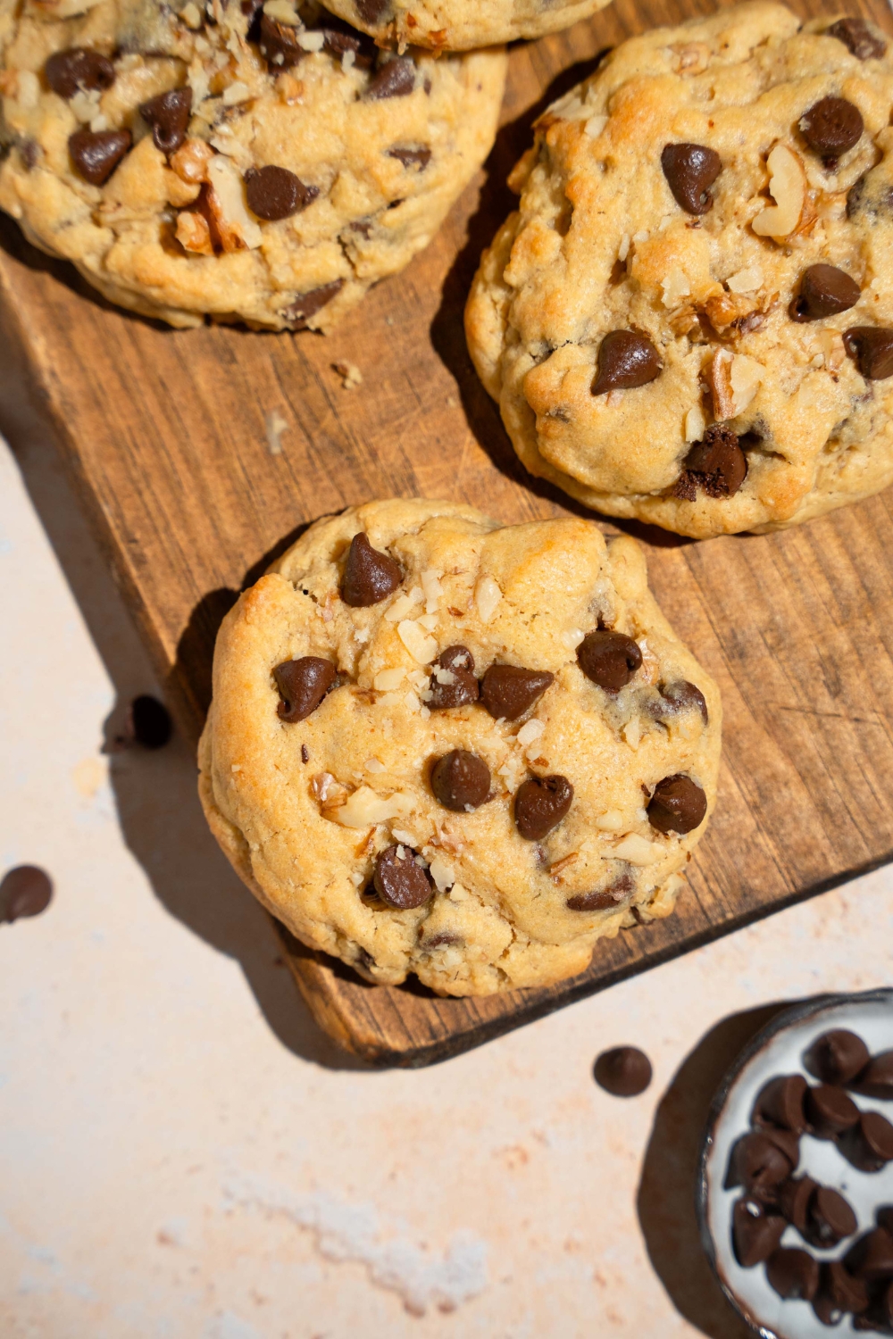 A Neiman Marcus chocolate chip cookie on a wooden board with additional cookies. The board is on a tan counter.