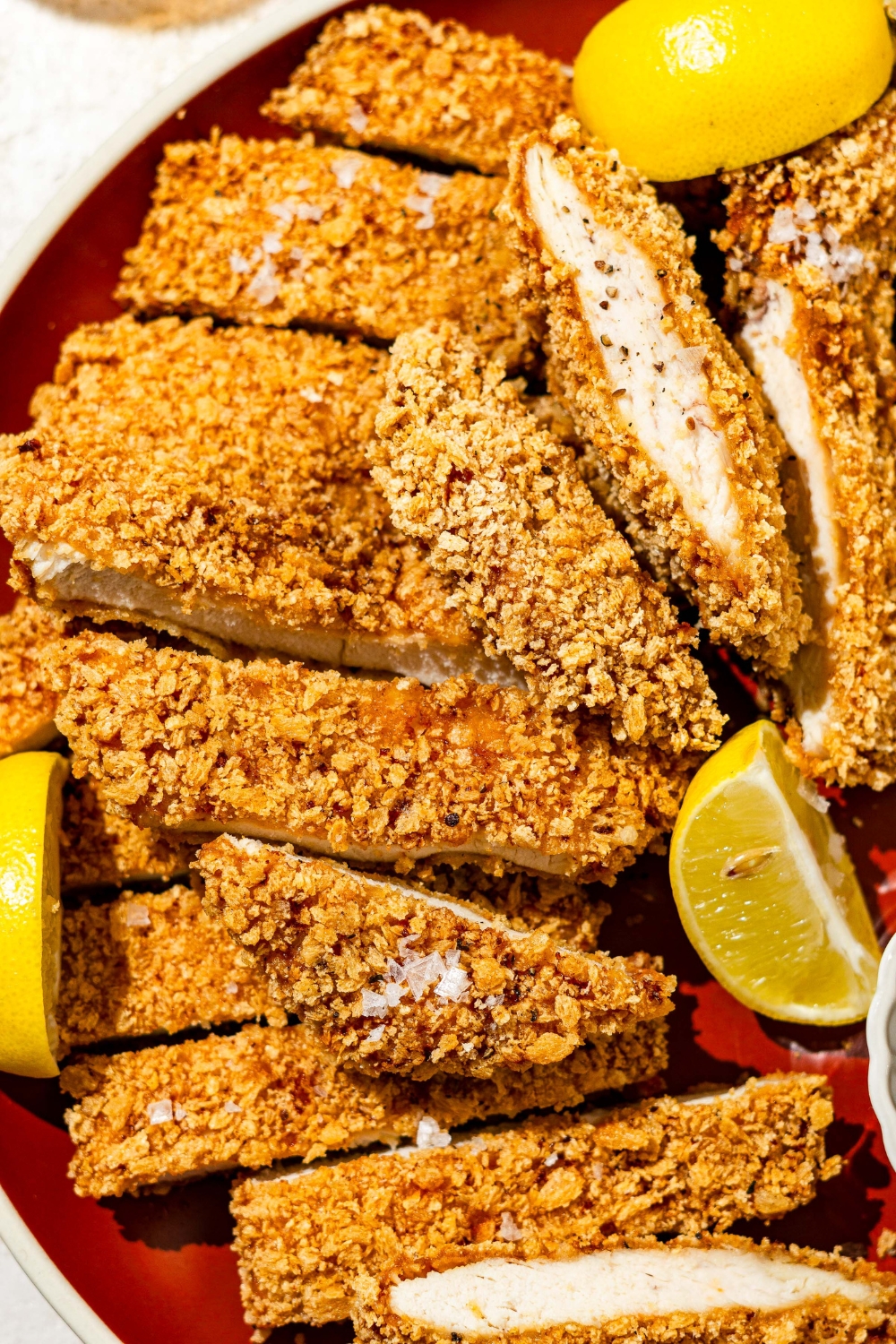 A plate of crispy chicken Katsu sliced in strips. The plate is garnished with lemon wedges.
