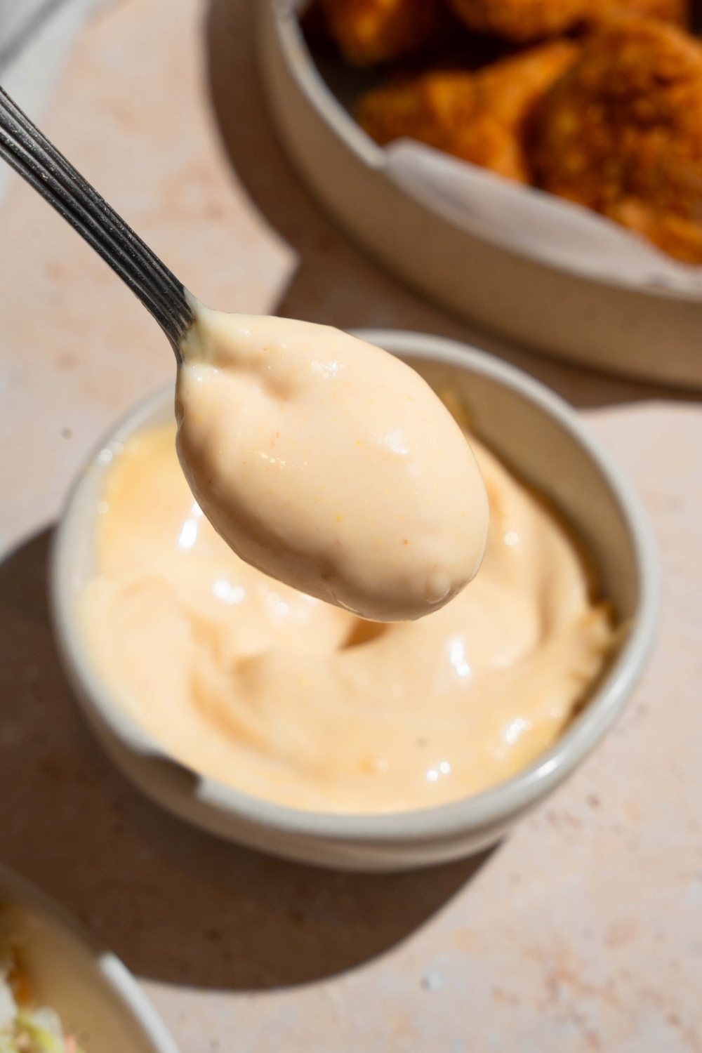 A close up of a spoon coated with homemade Chick Fil A sauce with a bowl of sauce blurred in the background.
