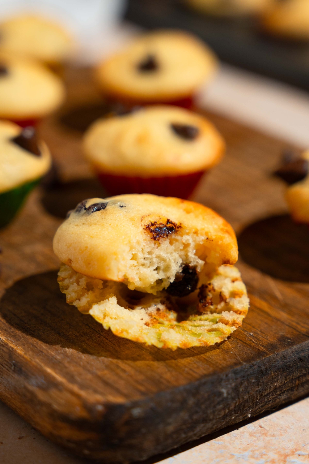 A wooden board with copycat Little Bites chocolate chip muffins. One of the muffins has a bite taken from it.