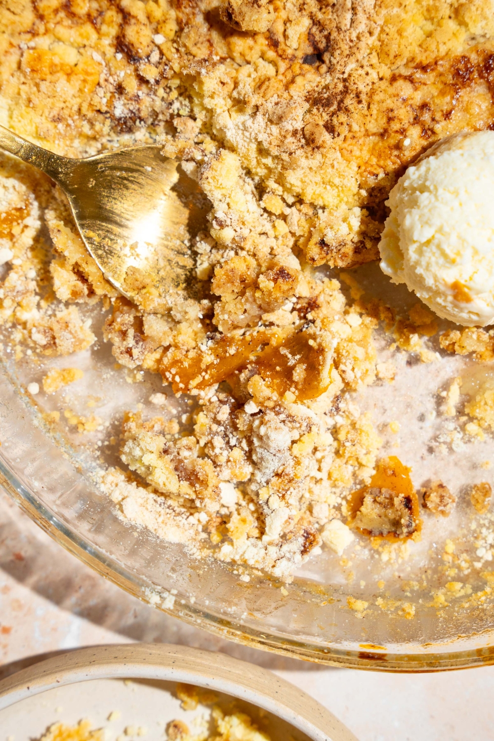 A glass baking dish with peach cobbler dump cake topped with a scoop of vanilla ice cream. There is a spoon in the dish.