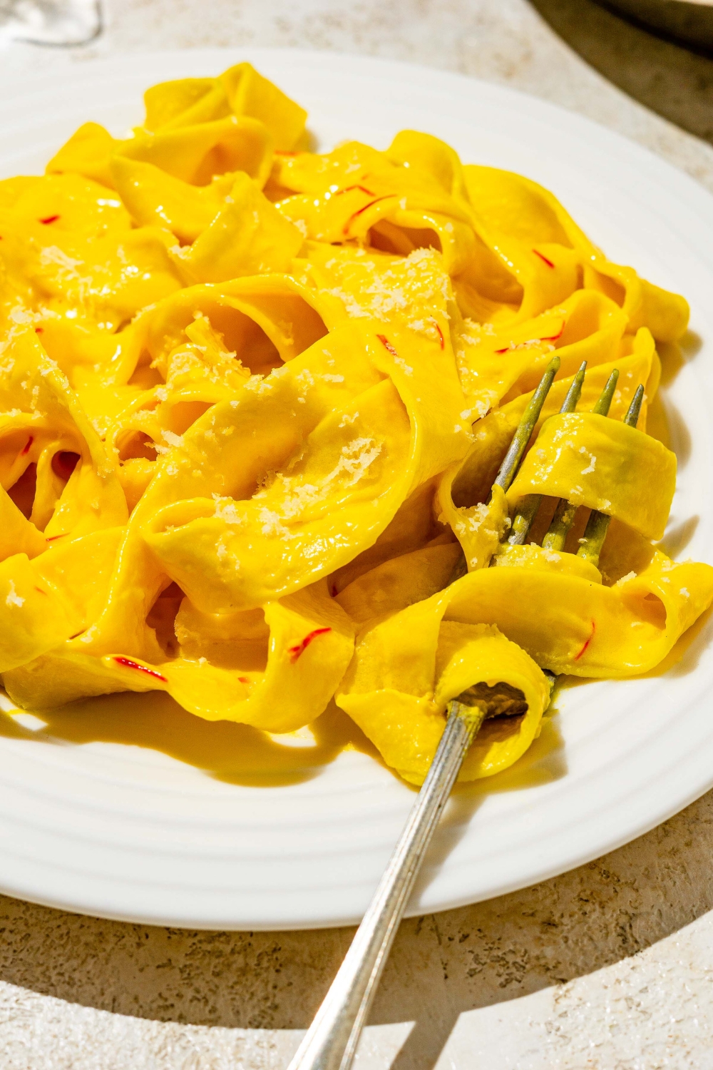 A white plate with fettuccine pasta tossed in saffron cream sauce. A fork has a bite of pasta twirled around it.