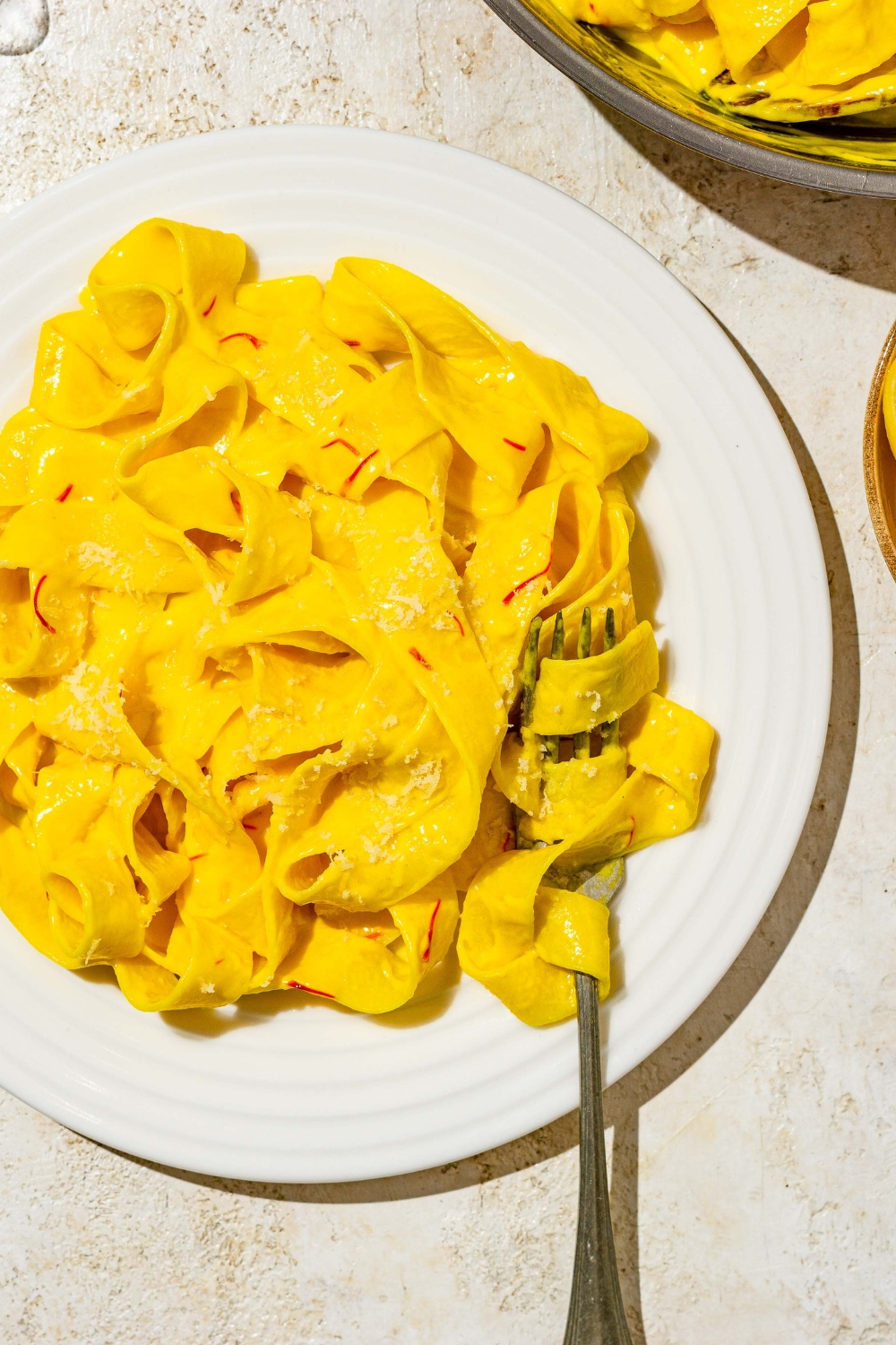 A white plate with fettuccine pasta tossed in saffron cream sauce. A fork has a bite of pasta twirled around it. The plate is on a tan counter.