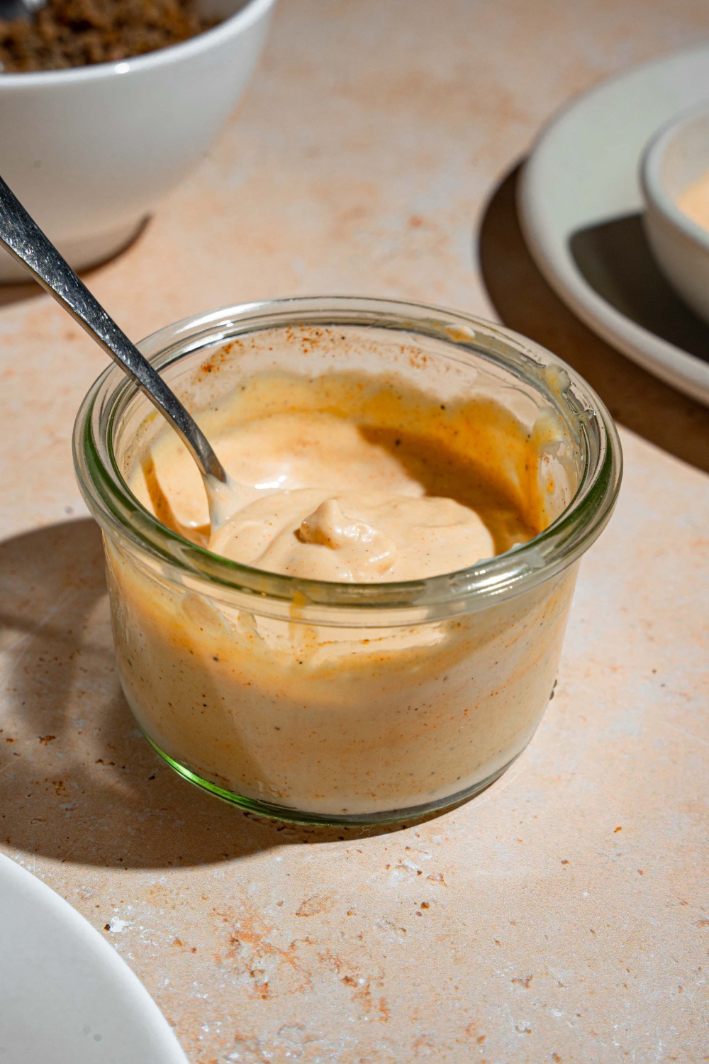 A glass jar with smash burger sauce with a spoon in the jar. The jar is on a tan counter with a white plate.