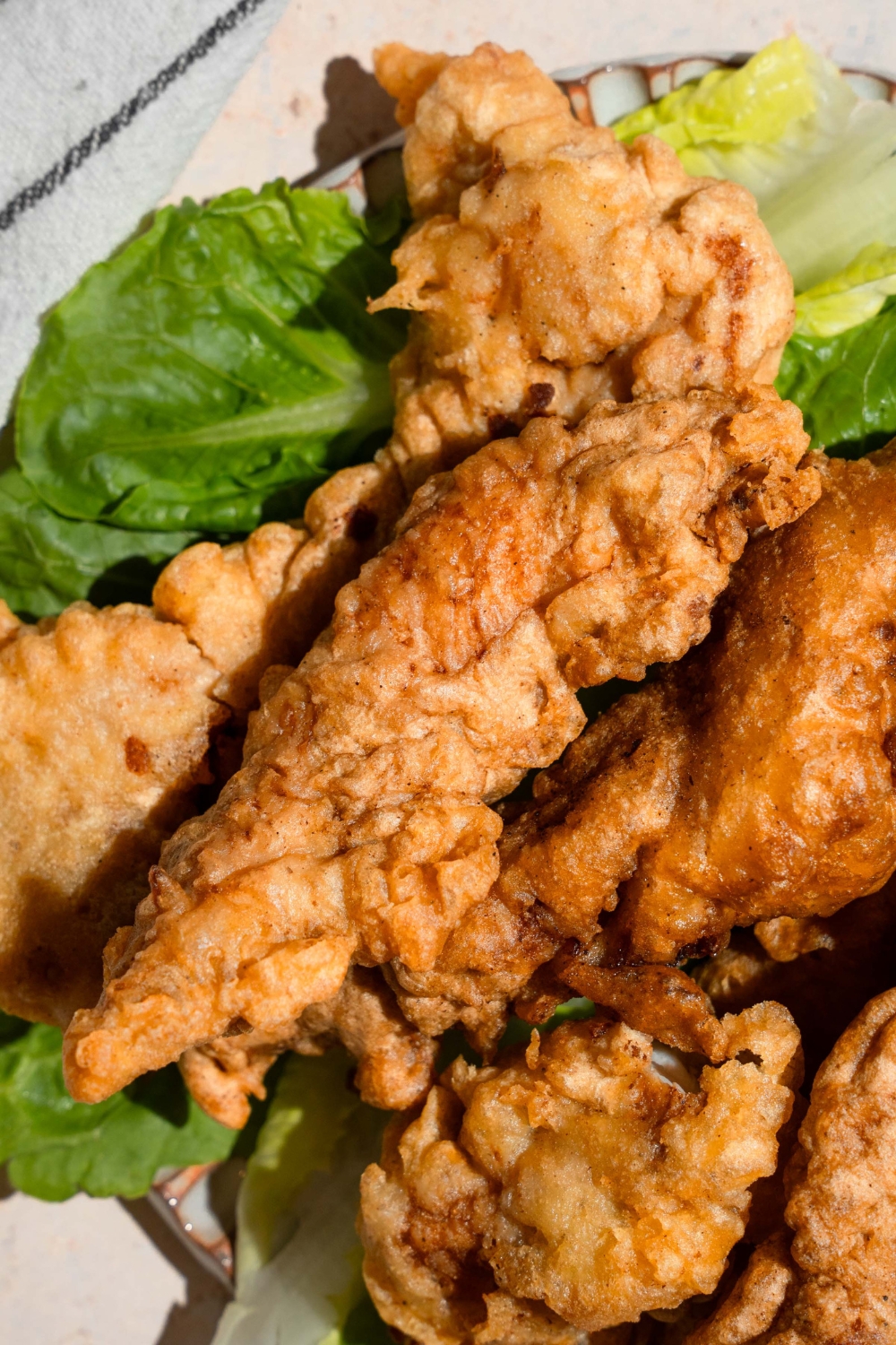 A ceramic plate with chicken tempura served over a leaf of lettuce. The plate is on a tan counter.