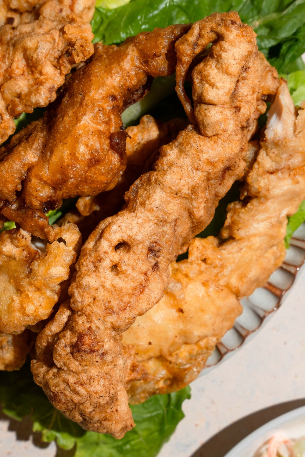 A ceramic plate with chicken tempura served over a leaf of lettuce. The plate is on a tan counter.