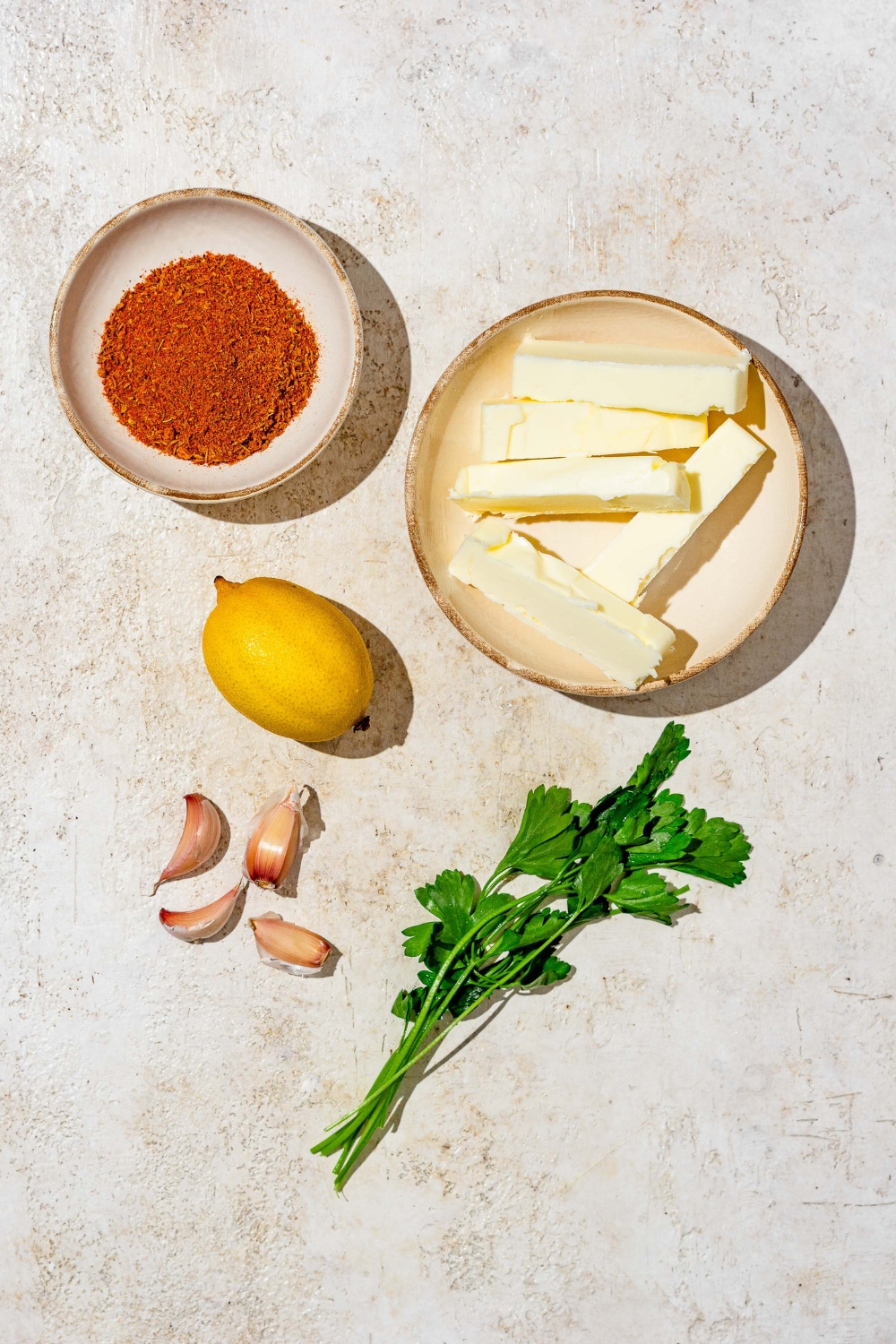 An overhead shot of several ingredients for cajun garlic butter sauce including butter, lemon, cajun seasoning, and parsley.