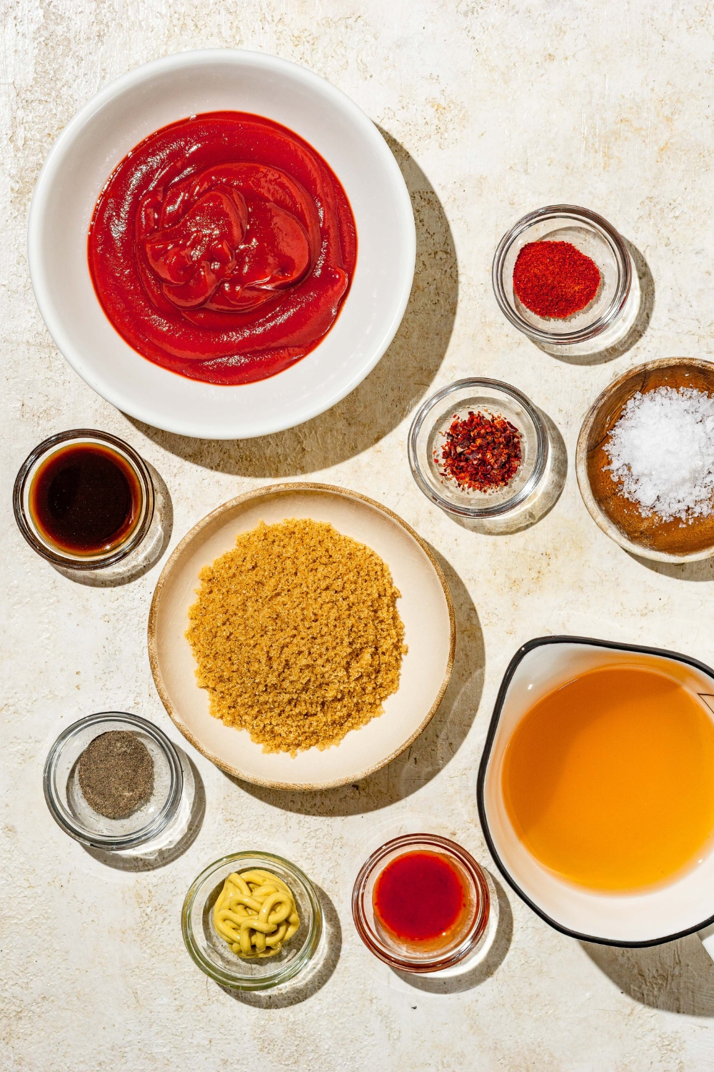 An overhead shot of several bowls in various sizes containing ingredients to make Carolina BBQ sauce including ketchup, apple cider vinegar, mustard, worcestershire sauce, hot sauce, salt, brown sugar, and seasonings.