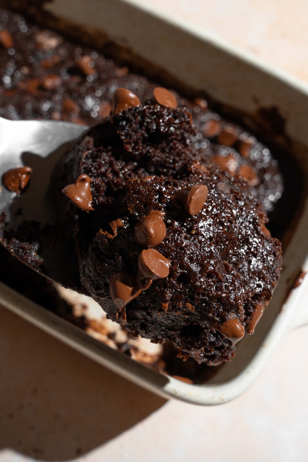 A baking dish with chocolate dump cake. A spoon is taking a bite of cake.