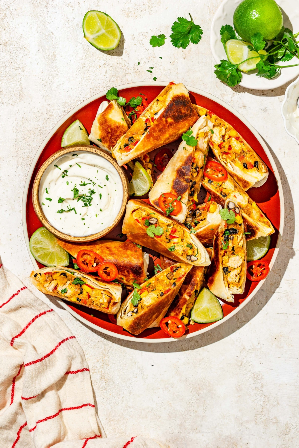A plate of copycat Chili's southwestern egg rolls sliced in half and garnished with sliced peppers, fresh cilantro, and lime. The plate is served with a small bowl of sour cream.