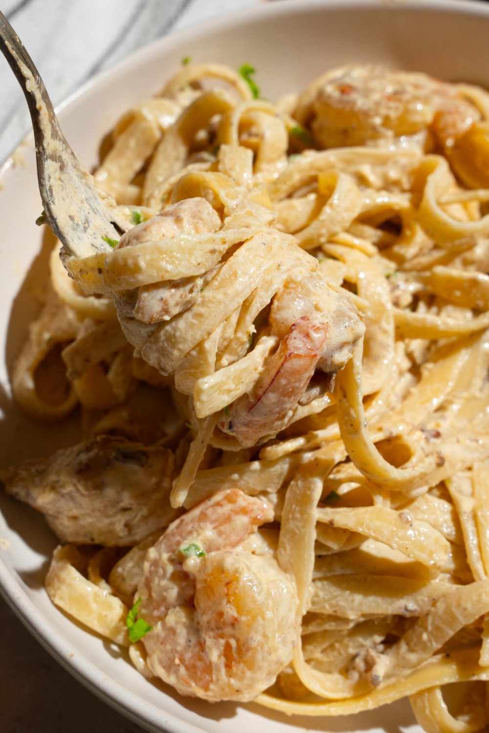 A bowl of chicken and shrimp alfredo garnished with fresh parsley. There is a fork taking a bite of pasta.