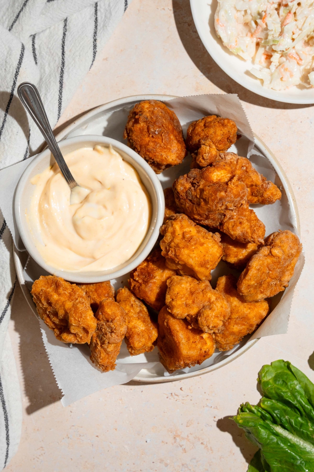 Homemade Chick Fil A nuggets and sauce on a plate lined with parchment paper. The plate is on a tan counter with a white striped napkin and small plate of coleslaw.