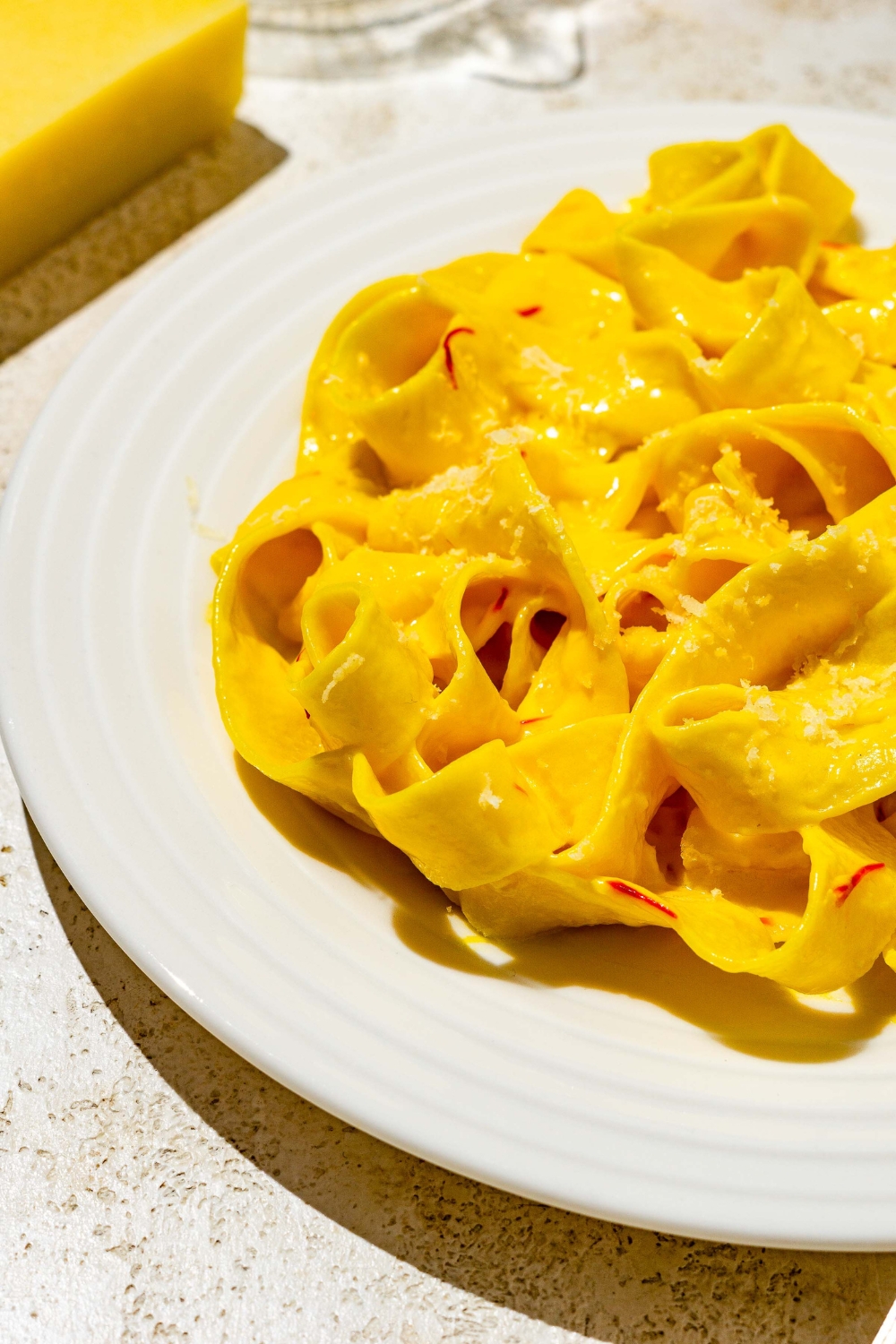 A white plate with fettuccine pasta tossed in saffron cream sauce. The plate is on a tan counter.