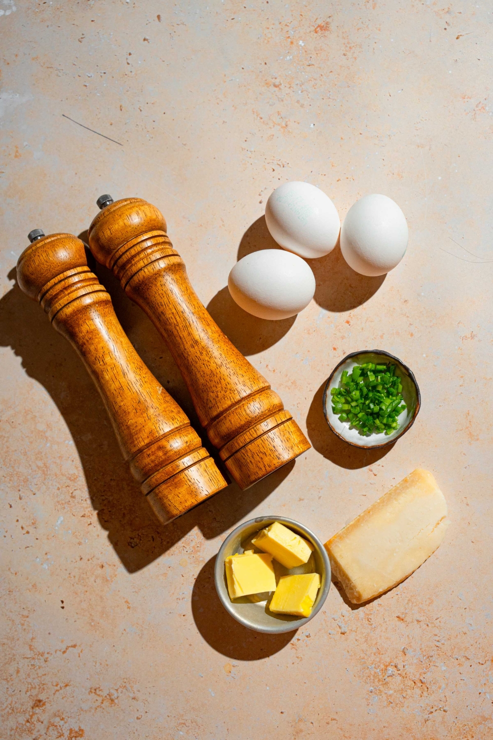 An overhead shot of ingredients to make Gordon Ramsay scrambled eggs including eggs, butter, parmesan cheese, chives, and a salt and pepper mill.