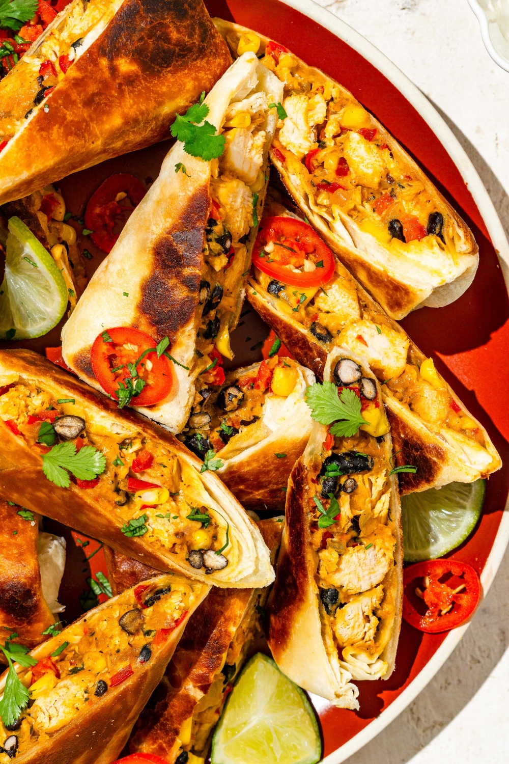 A plate of copycat Chili's southwestern egg rolls sliced in half and garnished with sliced peppers, fresh cilantro, and lime.