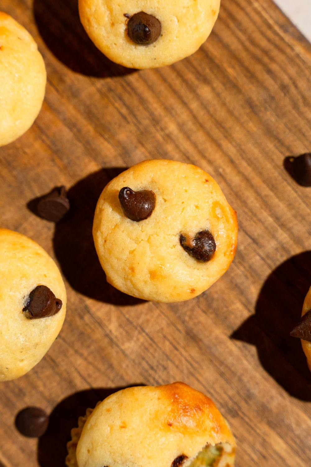 A wooden board with copycat Little Bites chocolate chip muffins. The board is garnished with chocolate chips.